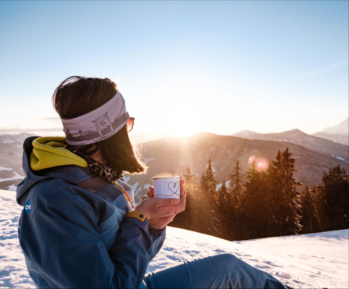 Winterwanderin mit heißem Getränk bei Sonnenaufgang über den Bergen